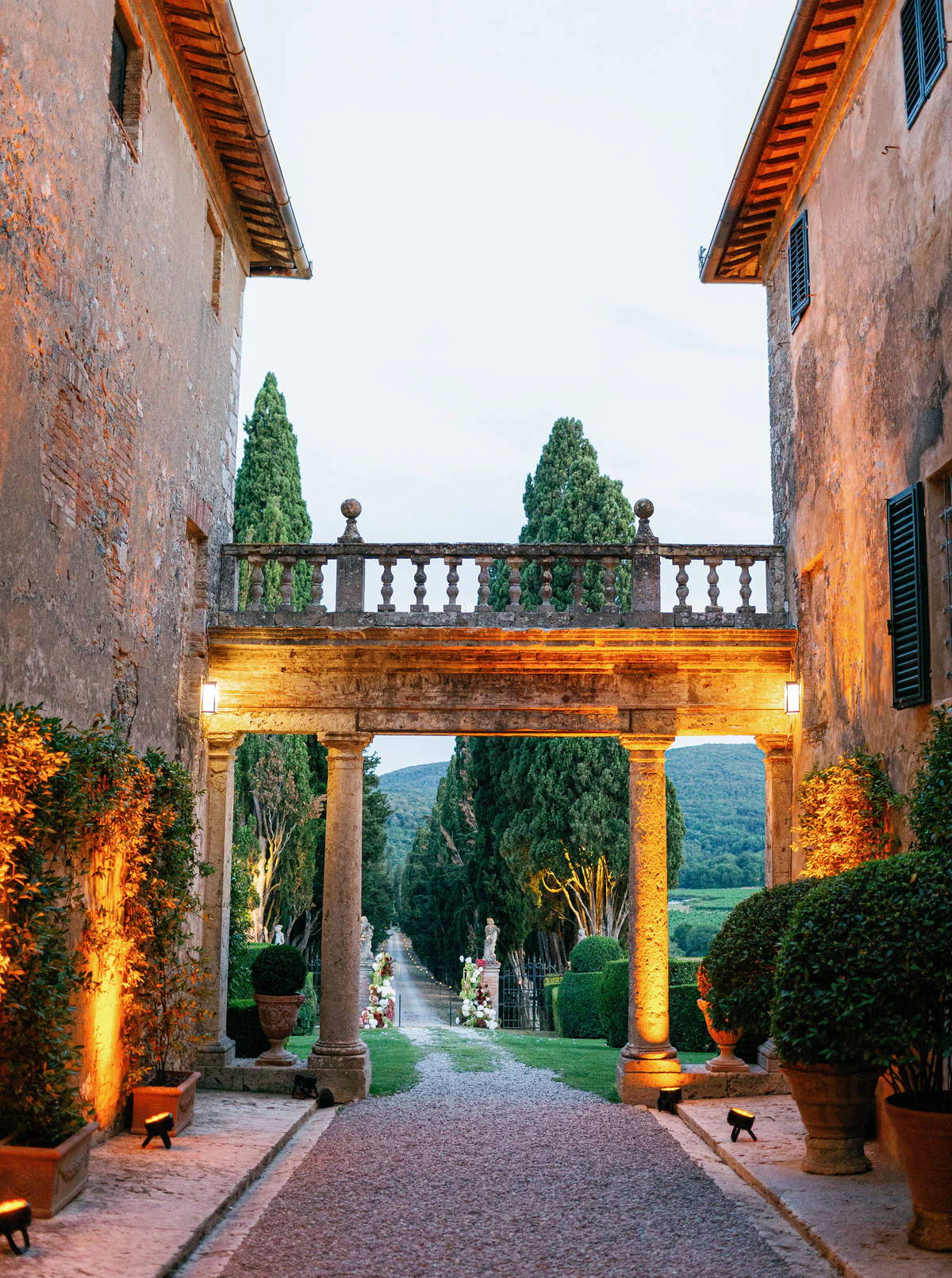 Lit stone loggia of Borgo Stomennano at dusk opening onto the cypress avenue, Chianti