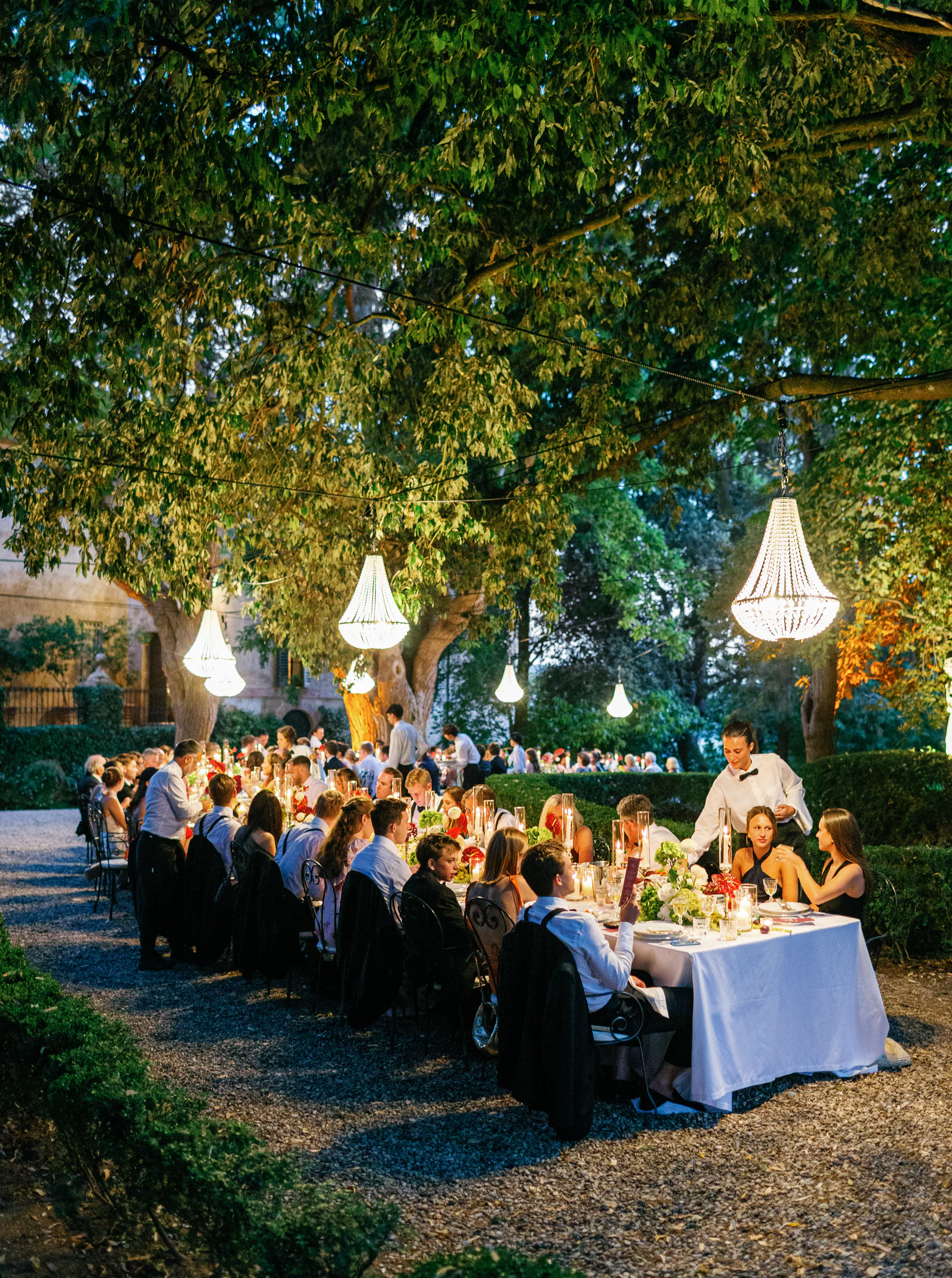 Guests at the long dinner table under crystal chandeliers at dusk, Borgo Stomennano, Chianti