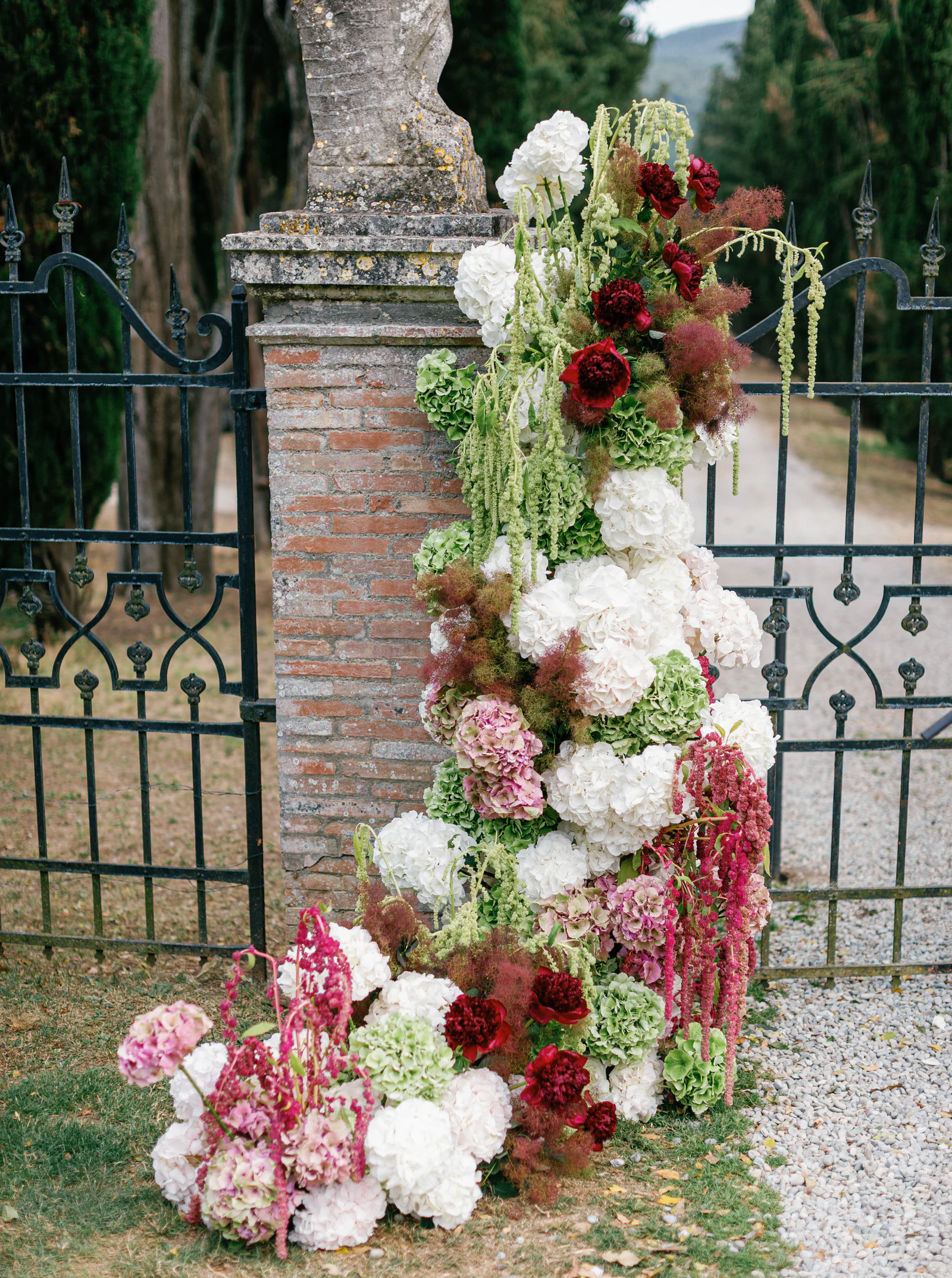 Stone gate pillar dressed with crimson and white blooms at Borgo Stomennano, Chianti, Tuscany