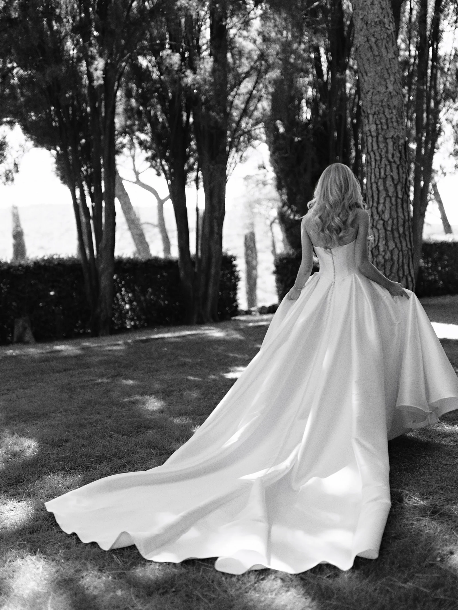 Bride's train trailing under the trees of Castiglion del Bosco, A Rosewood Hotel, in black and white, Tuscany
