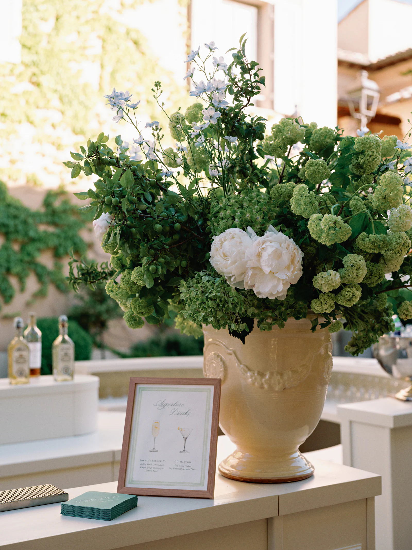 Peonies, viburnum and blue delphinium in a glazed Anduze urn beside the signature drinks card at the welcome party bar, Castiglion del Bosco, A Rosewood Hotel, Tuscany